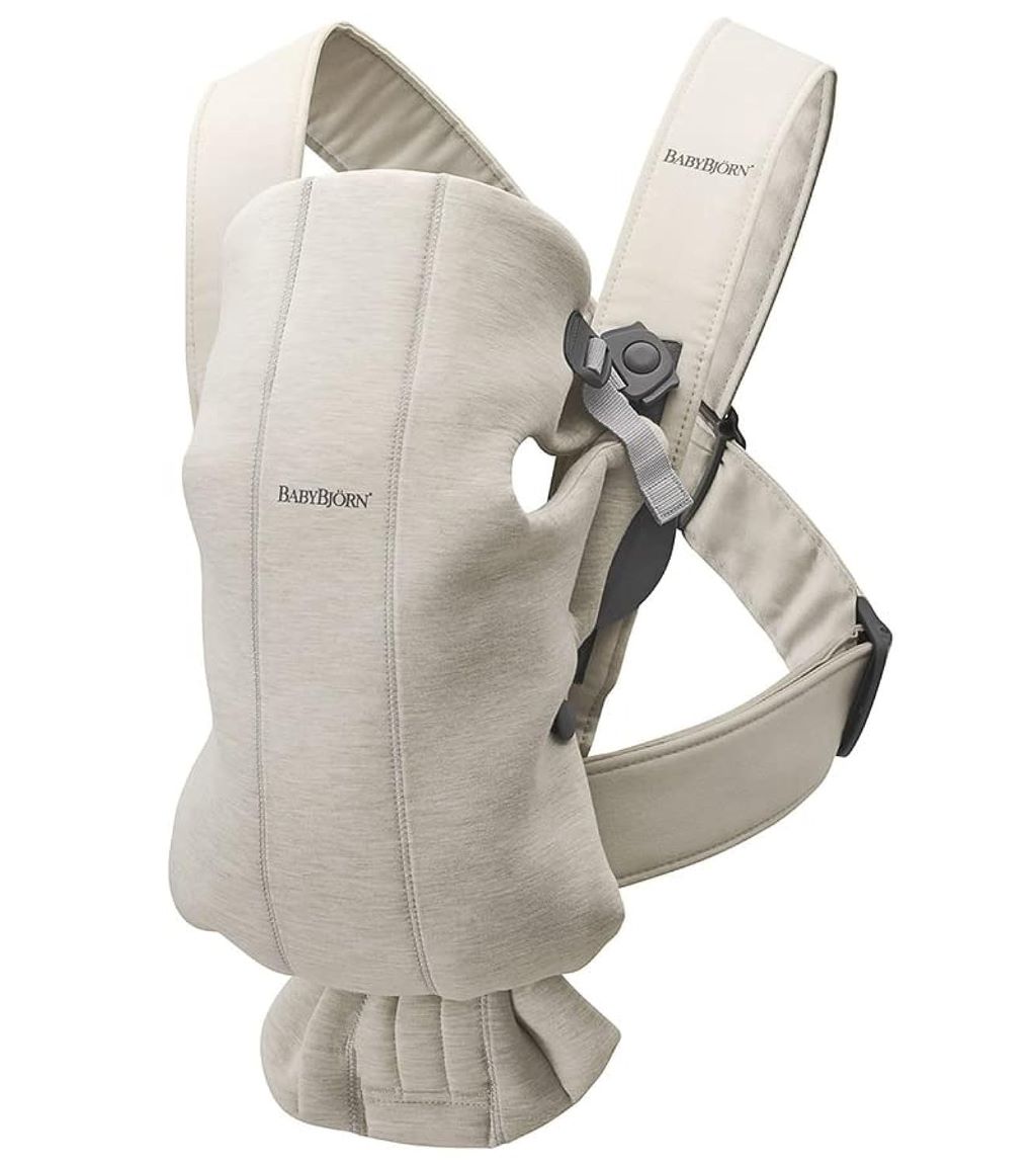 Parent wearing BabyBjörn Mini Carrier in light beige holding a newborn