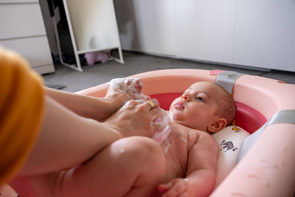 Baby Being Gently Bathed in a Pink Tub by a Caring Parent